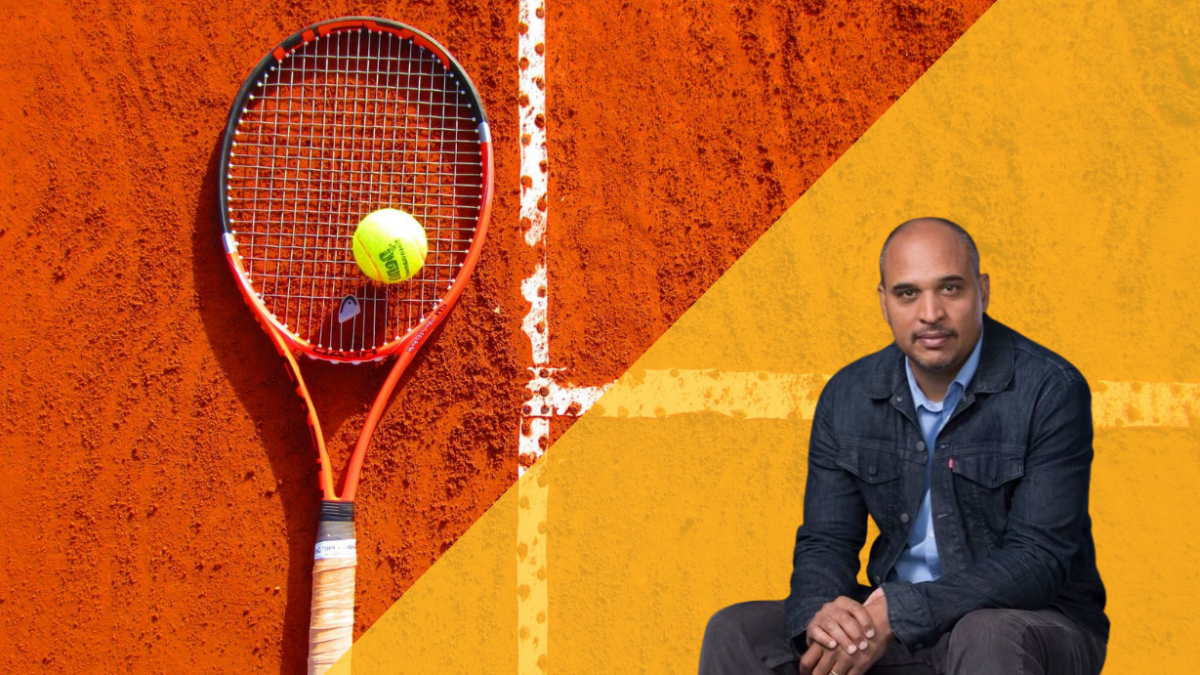 A tennis racket and ball on an orange court. 